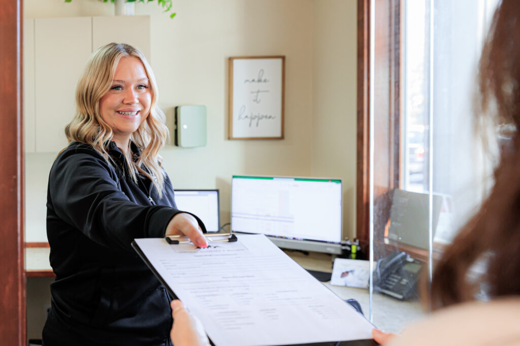 A provider smiles with a patient as she provides the check-in forms for hormone replacement therapy near Hayden