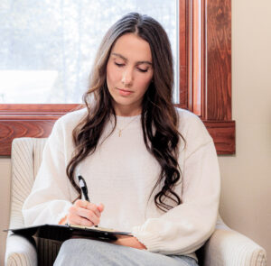 A woman with long hair dressed in a sweater fills out a form before entering a consultation for FormaV treatment in Coeur d’Alene.